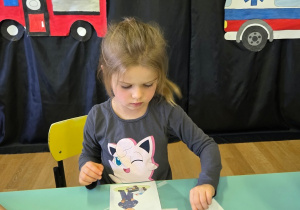 Dziewczynka dopasowuje numery alarmowe do ilustracji.