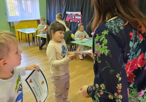 Przedszkolaki odbierają dyplomy od nauczyciela.