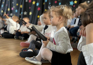 Dzieci siedzą na podłodze i trzymają rekwizyty potrzebne do występu.