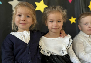 Dwoje dzieci uśmiecha się i obejmuje na tle dekoracji z gwiazdkami.