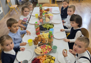 Poczęstunek: dzieci przy stole z owocami, napojami i przekąskami.