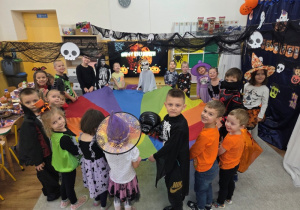 Dzieci stoją wokół kolorowej chusty animacyjnej; wkoło widać różne halloweenowe kostiumy i uśmiechnięte twarze.