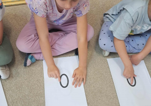 Dziewczynka recytując wierszyk rysuje palcem wskazującym po kartce literkę O.