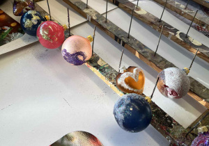 Rząd gotowych, błyszczących bombek w różnych kolorach suszy się na specjalnym stojaku.