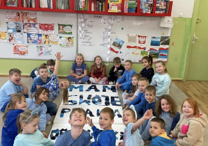 Grupa dzieci siedzi wokół dużego napisu „MAM SWOJE PRAWA” ułożonego z materiałów i pozują do zdjęcia.