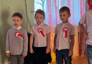 Kilkoro dzieci stoi obok siebie, gotowe do występu; wszystkie ubrane w białe koszule z kotylionami.