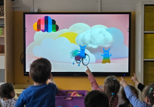 Dzieci oglądają na ekranie animację o prawach dziecka i wskazują elementy na ekranie.