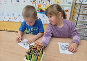 Dwójka dzieci koloruje obrazki siedząc przy stoliku.