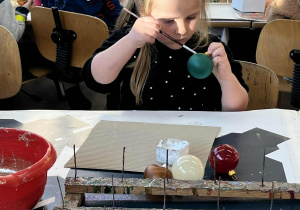 Dziewczynka maluje bombkę.