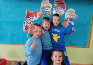 Czwórka dzieci pozuje do zdjęcia na tle obrazków przedstawiających smerfy.