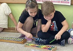 Klara i Antek uderzają młoteczkiem w metalowe płytki dzwonków chromatycznych na których naklejone zostały litery.