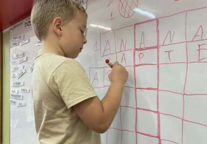 Chłopiec zapisuje na tablicy sucho ścieralnej słowo w krzyżówce.