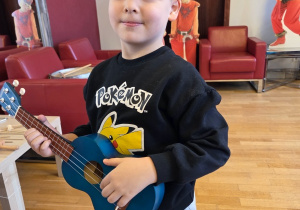 Dziecko trzyma małe ukulele podczas zajęć muzycznych.