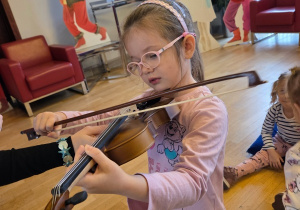 Dziecko gra na skrzypcach z pomocą osoby dorosłej.