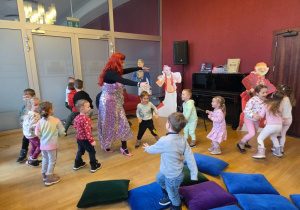Dzieci tańczą i bawią się w rytm muzyki z prowadzącą.