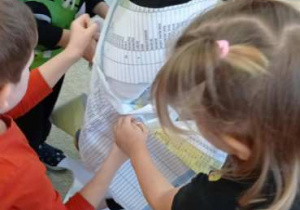 Dzieci owijają jednego z kolegów papierem, tworząc przebranie mumii.