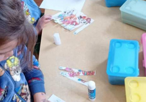 Dziewczynka układa i przykleja kawałki puzzli zgodnie z kolejnością cyfr.