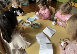 Zdjęcie przedstawiające dzieci robiące bombki ze styropianu i cekinów przy stoliku.