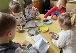 Zdjęcie przedstawiające dzieci robiące bombki ze styropianu i cekinów przy stoliku.