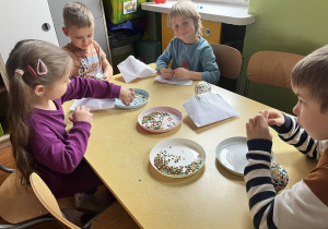 Zdjęcie przedstawiające dzieci robiące bombki ze styropianu i cekinów przy stoliku.