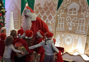 Dzieci obejmują Świętego Mikołaja, trzymając w rękach otrzymane prezenty.