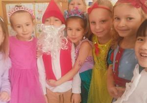 Grupa dzieci stoi razem i pozuje do zdjęcia. Przedszkolaki są ubrane w kolorowe, bajkowe stroje, m.in. księżniczek i krasnoludka. Dzieci uśmiechają się i obejmują.