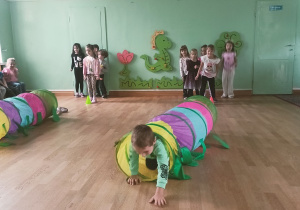 Chłopiec przechodzi przez kolorowy tunel jako element toru przeszkód. W tle grupa dzieci czeka na swoją kolej.