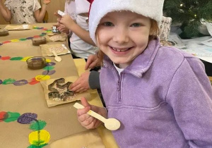 Dziewczynka w czapce mikołaja w trakcie warsztatów pozuje do zdjęcia.