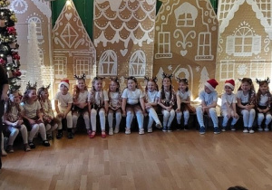 Dzieci w świątecznych strojach siedzą na ławce.