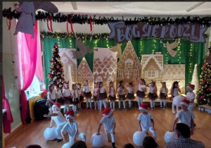 Chłopcy w czapkach mikołaja wykonują układ z użyciem dmuchanych piłek plażowych.