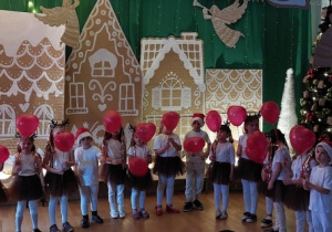 Dzieci stoją trzymając w rękach czerwone balonowe serduszka.