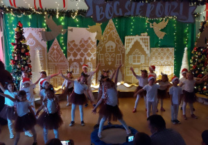 Dzieci tańczą w rytm muzyki podczas bożonarodzeniowego przedstawienia.