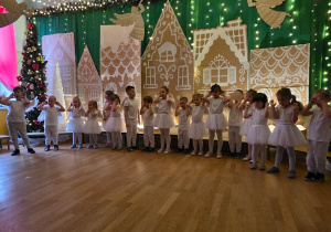 Dzieci stoją na scenie i wykonują gesty do piosenki świątecznej.