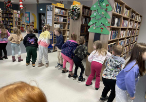Dzieci wykonują zabawę muzyczno-ruchową między regałami w bibliotece.