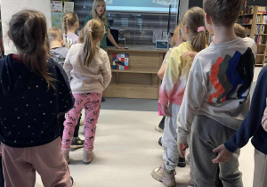 Dzieci słuchają prowadzącej podczas zajęć w bibliotece.