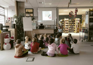 Dzieci siedzą i słuchają opowiadania w bibliotece.