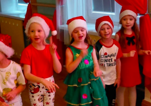 Dzieci ubrane na świątecznie stoją razem, uśmiechają się i biorą udział w spotkaniu z Mikołajem.