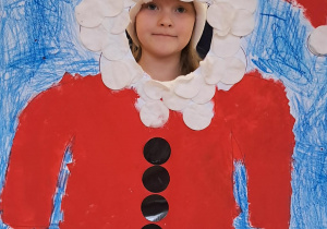 Dziecko uśmiecha się, pozując w świątecznej dekoracji z Mikołajem.