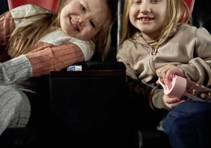 Dwie dziewczynki siedzą w fotelach kinowych i uśmiechają się przed seansem.