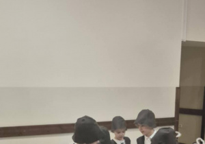 Chłopcy przebrani za pasterzy odgrywają scenę jasełkową, w tle siedzą dzieci.