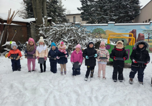 Grupa dzieci stoi w rzędzie na śniegu, każde trzyma tackę do malowania.