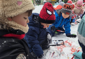 Kilkoro dzieci maluje śnieg kolorowymi farbami na dworze.