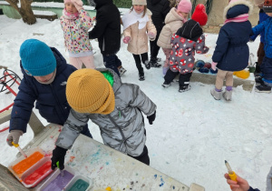 Dzieci nabierają kolorową wodę pipetami i barwią śnieg.