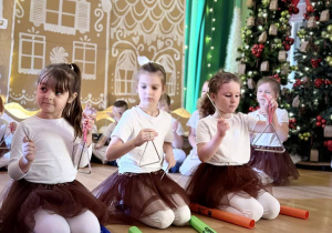 Dzieci klęczą na scenie i grają na instrumentach perkusyjnych podczas występu.