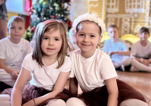 Dwie dziewczynki siedzą na podłodze przed dzwonkami muzycznymi i uśmiechają się do aparatu.