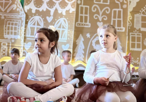 Dziewczynki siedzą na podłodze z instrumentami muzycznymi podczas występu.