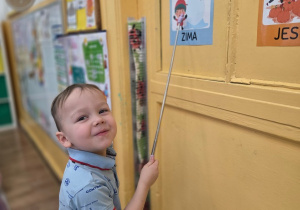 Dziecko wskazuje obrazek z napisem „zima” na drzwiach w sali przedszkolnej.