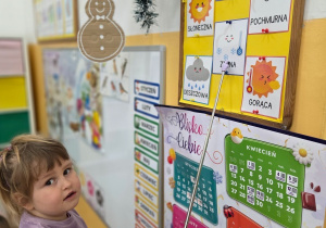 Dziecko pokazuje wskaźnikiem tablicę z informacją o pogodzie.