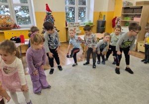 Grupa dzieci wykonuje ćwiczenia ruchowe na dywanie w sali.