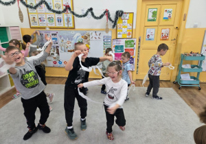 Dzieci tańczą i poruszają się z białą bibułą w sali.